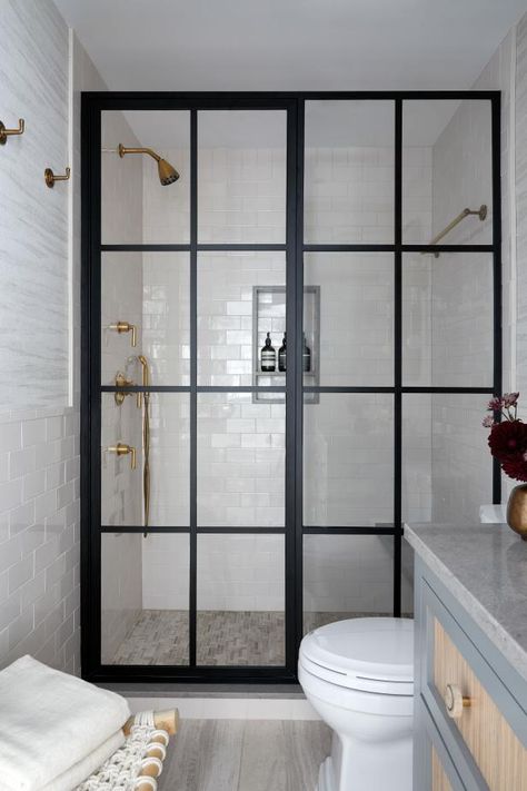 This neutral transitional bathroom is lined with classic subway tile and subtly patterned wallpaper. It’s the shower that’s the center of attention, though, thanks to black-framed glass doors with multiple panes. Gold-colored fixtures add some glam to the space. Black Bathroom Fixtures, Black Shower Doors, Bathroom Shower Doors, Framed Shower Door, Subway Tiles Bathroom, Transitional Bathroom, Modern Farmhouse Bathroom, Black Shower, Glass Shower Doors