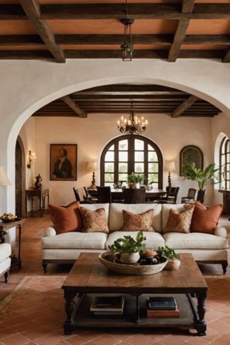 Cozy living room with white sofas and orange pillows, wooden coffee table, arched doorways, and exposed wooden beams on the ceiling. Mexico Style Living Room, Modern Spanish Revival Living Room, Living Room Decor Spanish Style, Spanish Colonial Style Homes Interior Living Room, Spanish Colonial House Interior Design, Classic Spanish Interior Design, Spanish Style Couch, Saltillo Floor Living Room, Spanish Style Interior Design Living Room