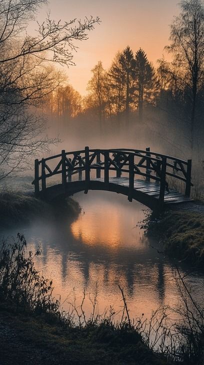 In the early hours of the morning, a wooden bridge casts a delicate silhouette over a quietly flowing river. The mist, suffused with the warm glow of sunrise, creates an ethereal atmosphere that softens the landscape. Surrounding trees, partially obscured by the fog, add a sense of mystery and depth to the tranquil scene, inviting a moment of peaceful reflection. Mist Landscape, Morning Flow, Beach Silhouette, Fog Photography, Architecture References, Sunrise Images, Flowing River, Misty Morning, Stone Bridge