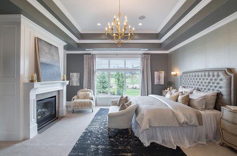 Chic gray bedroom features overlapped tray ceilings accented with a brass tiered chandelier illuminating an accent wall clad in gray geometric wallpaper lined with a gray tufted headboard on bed dressed in platinum gray bedding and a white tulle bedskirt flanked by curved 3 drawer nightstands alongside a cream couch placed at the foot of the bed atop a black overdyed rug. Bedroom Tray Ceiling, Luxury Bedroom Master, Beautiful Bedroom, Master Bedrooms Decor, Modern Bed, Dream Rooms, Beautiful Bedrooms, Dream Bedroom, Design Case