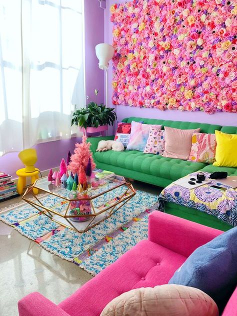 a maximalist living room with purple walls, a bright green and pink sofa, colorful pillows, a glass coffee table and a bright flower wall Colorful Beauty Room, Lisa Frank Office, Colorful Witchy Decor, Barbie Core Room, Colourful Eclectic Interiors, Vintage Colorful Home Decor, Colourful Living Room Decor Small Spaces, Colourful Room Ideas, Studio Mucci