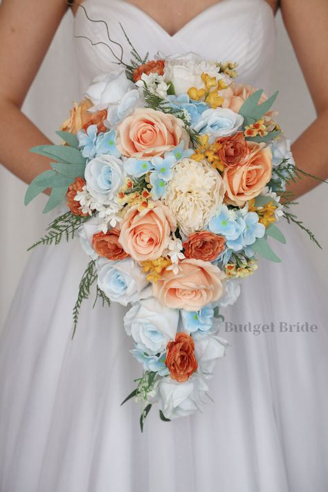 This lovely assortment of peach, terracotta, light blue and cream roses is bound to turn heads on your wedding day. This lovely cascading brides’ bouquet from the is an absolutely breathtaking arrangement for any bride to be, in any season. Sage greenery and yellow accents complete the look and add a delicate realism to this beautiful bouquet. This bouquet is 10” wide, 18” long, and is crafted by our in-house florists without using a foam base to anchor the flowers to the bouquet. Instead, we wi Peach And Sky Blue Wedding, Terracotta And Light Blue Wedding, Dusty Blue And Coral Wedding, Wedding Bouquets Spring, Peach Terracotta, Small Bridesmaid Bouquets, Fake Wedding Flowers, Sage Eucalyptus, Homestead Wedding