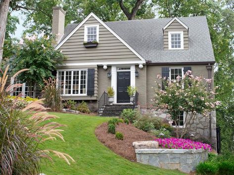 Cape Cod style -- house colors & landscaping - retaining walls of stone, brick or concrete can shore up the layers of a sloping yard & define flower beds: main bed, bordered by a granite retaining wall, is filled w/ purple 'Wave' petunias; fountain grass grows near the large front window. Crepe myrtles bloom all summer long & are beautiful & low-maintenance - HGTV Tan House, Black Shutters, Gray House, Casas Coloniales, Exterior Paint Colors For House, White Windows, Casa Exterior, Painted Brick, Garden Landscape Design