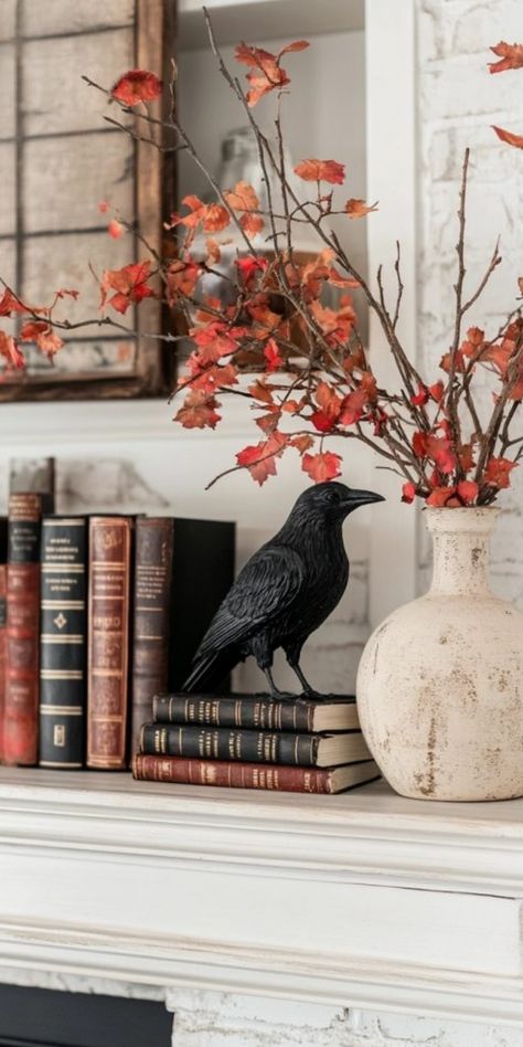 Decorative raven statue on stacked books with fall foliage in a white vase on a mantel. Fall Halloween Shelf Decor, Halloween Decor Floating Shelves, Spooky Mantel Ideas, Seasonal Mantle Decor, Halloween And Thanksgiving Decor, Spooky Elegant Halloween, Halloween Decor For Coffee Table, Halloween Mantels Ideas, Elegant Halloween Decor Living Room