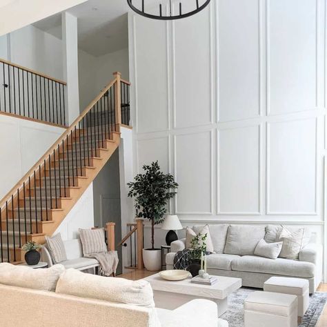 This bright and airy living room features a warm wooden staircase with black iron spindles and a gray carpet runner. Tall, paneled walls draw the eye upwards towards the second floor. Comfortable neutral couches are centered around a rectangular white oak coffee table, creating a relaxing and modern space. Modern Wood Stairs, Bright And Airy Living Room, Modern Farmhouse Staircase, Wood Paneling Living Room, Airy Living Room, White Oak Coffee Table, Iron Spindles, Living Room Panelling, Gray Carpet