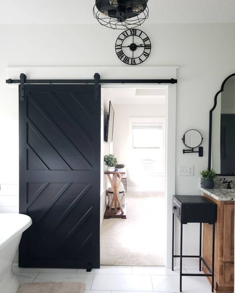 Black bathroom side table stands on white and gray marble floor tiles. A black chevron sliding barn door on black rails is opened to reveal a stained wood console table under a wall mounted TV. Black Barn Door Bedroom, Grey Barn Door, Sliding Restroom Door, Black Barn Doors Sliding, Black Sliding Barn Door, Barn Door Black, Black White And Grey Basement Ideas, Modern Farmhouse Barn Door, Black Barn Doors In The House