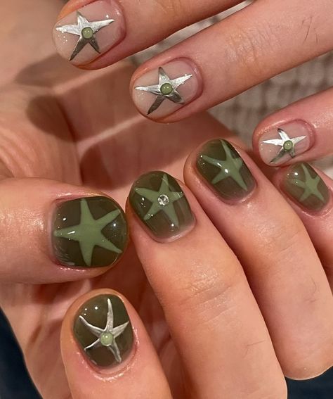 Embrace the fall season with these chic Fall Green and Silver Nails, showcasing an olive green base and elegant silver stars for a stylish yet simple design.  🍂 Recreate this look yourself with our Korean Gel Nail Polish collection!  🍂 Credit: y_yjenny on Instagram 🍂 Fall nails, green fall nails, short fall nails, jelly nails, korean fall nails, korean jelly nails, green nails, silver stars nails, fall nail design, olive green nails, chic nail art, simple nail design, seasonal nails, autumn nails, Korean gel polish, trendy nails, nail art ideas, nail inspiration, stylish nails, elegant nails, manicure trends, fall manicure Green And Silver Nails Short, Green Fall Nails Short, Silver Stars Nails, Fall Gel Nail Colors, Silver Nails Short, Green And Silver Nails, Fall Nails Green, Korean Jelly Nails, Gel Nail Polish Brands