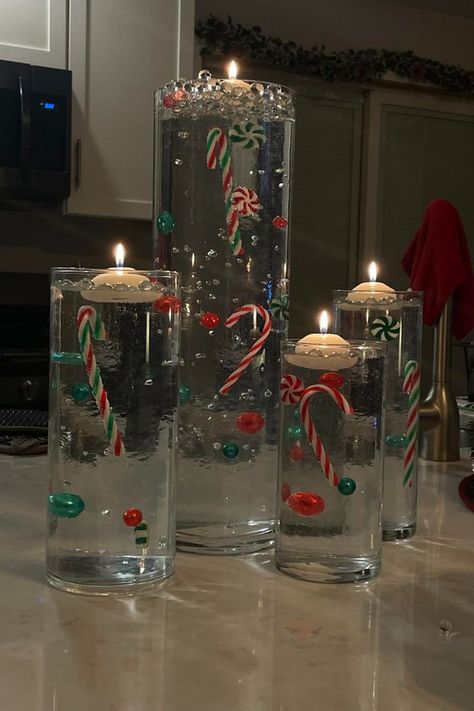 Orbeez Christmas vase with floating candles on top. Inside the four vases the decorations appear to float due to clear orbeez decor. There are candy canes and green and red ornaments in the vases for a Christmas centerpiece. Orbeez Christmas Decor, Floating Candles Christmas, Unique Christmas Decorations Diy, Diy Orbeez, Christmas Floating Candles, Diy Christmas Vases, Water Beads Centerpiece, Floating Candle Centerpieces Diy, Floating Candles Halloween