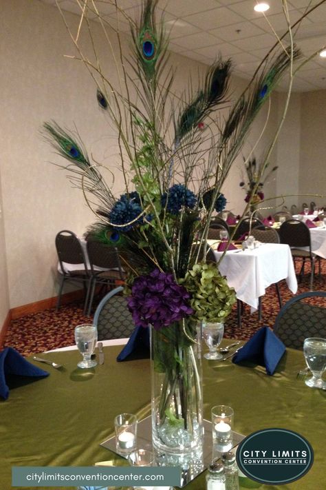 Add a touch of peacock to your wedding or event. Use this centerpiece or a variation of it for your decorations at the City Limits Convention Center located in Colby KS. This piece features dark blue and purple. The peacock color palatte was an inspiration for this certerpiece. You can rent this piece on-site or off-site at City Limits Convention Center. www.citylimitsconventioncenter.com #peacockthemedwedding #weddingdecorations #weddingcenterpiece #citylimitsconventioncenter Centerpieces Non Floral, Wedding Centerpieces Unique, Peacock Wedding Centerpieces, Unique Wedding Centerpieces, Centerpiece Diy, Floral Peacock, Peacock Wedding Theme, Peacock Theme, Unique Wedding Flowers