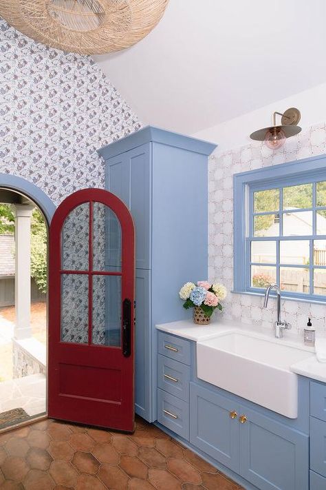 Cornflower blue mudroom features an arched red glass panel door, cornflower blue cabinets with brass pulls, a white apron sink lit by a vintage lantern on gray Moroccan tiles and terracotta arabesque floor tiles. Blue Laundry Room, White Apron Sink, Moroccan Wall Tiles, Blue Stripe Wallpaper, Transitional Laundry Room, Grey Laundry Rooms, Blue Laundry Rooms, Blue Subway Tile, Blue Shelves