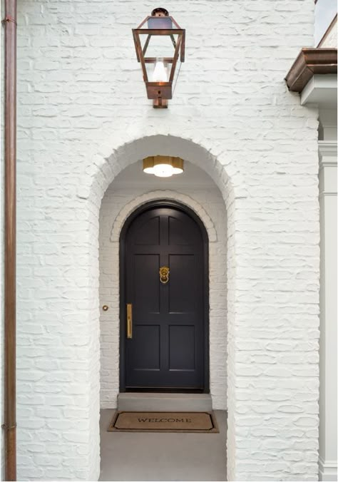 A white painted brick Tudor house with arched doorways, black front door, and copper downspouts. White Painted Brick Exterior, Arched Front Door, Painted Brick Exteriors, Painted Brick House, Timeless Interior Design, Brick Arch, Black Front Doors, Timeless Interior, Tudor Style Homes