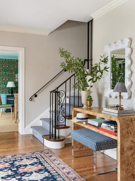 A red and blue rug sits in front of a blue stool placed beneath a burl wood waterfall console table, styled with stacked books and located under a white scalloped mirror. Burlwood Entry Table, Burlwood Console Table, White Scalloped Mirror, Entrance Foyer Design, Scalloped Mirror, Glam Pad, Vintage Bench, Small Entry, Entrance Foyer