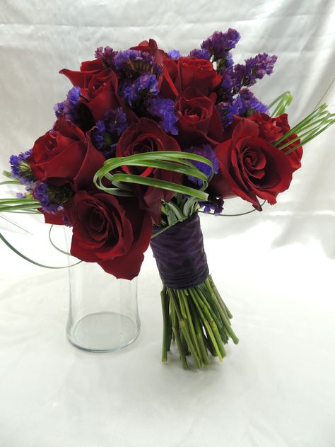 Bridal bouquet made of red roses and purple statice, with bear grass loops for an extra beautiful look. Red And Purple Rose Bouquet, Black Red And Purple Bouquet, Red Roses And Lavender Bouquet, Red And Purple Bouquet Wedding, Red Purple Bouquet, Dark Purple And Red Wedding Theme, Purple And Red Wedding Flowers, Lilac And Red Wedding, Red And Purple Flower Arrangements