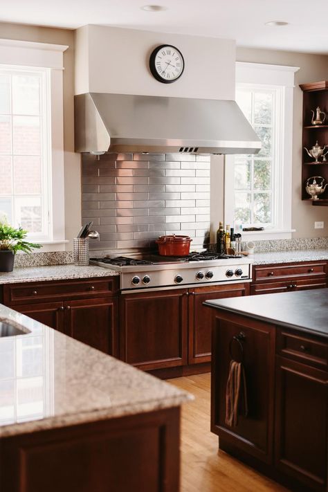 A sleek stainless steel subway tile backsplash is a nice complement to the stainless steel cooktop and range hood in this transitional kitchen. Traditional dark wood cabinets add contrast to the stylish design. Stainless Steel Tile Backsplash, Metallic Tiles, Average Kitchen, Easy Kitchen Updates, Kitchen Cabinets Upgrade, Kitchen Layouts With Island, Kitchen Cabinets Pictures, Oven Hood, Stainless Steel Backsplash