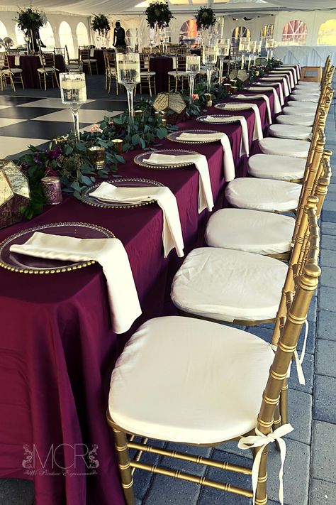 An elegant art deco themed wedding with burgundy linens and gold accents. An abundance of greenery lines the long head table, floating candles in wine glass vases and gold geometric lanters add both vintage and modern elements to the wedding decorations. Gold chiavari chairs with ivory cushions and napkins brighten the decor and match the black and white checkered dance floor. #dream #dreamwedding #centerpieces #reception #weddingreception #dancefloor #october #octobercolors Chivari Chairs Wedding, Wedding Decorations Gold, Art Deco Themed Wedding, Head Table Design, Checkered Dance Floor, Gold Chivari Chairs, Art Deco Wedding Theme, Gold Chiavari Chairs, Chiavari Chairs