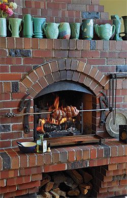 CREATE A UNIQUE KITCHEN WITH ONE-OF-A-KIND DETAILS: Right around the corner from the big island, a fireplace with a rotisserie is the perfect place to slow-roast a leg of lamb on a foggy San Francisco weekend. Weir hired San Francisco ironworker Jefferson Mack to customize the brick fireplace into a wood-burning indoor grill. A rotisserie motor mounted on the side of the fireplace turns a chain-driven spit cradled by forged-steel brackets. A pair of gas jets in the floor of the firebox makes ... Indoor Pizza Oven, Pizza Oven Fireplace, Fireplace Cooking, Outdoor Stone Fireplaces, Oven Fireplace, Fireplace Kits, Charcoal Grills, Leg Of Lamb, Outdoor Barbecue