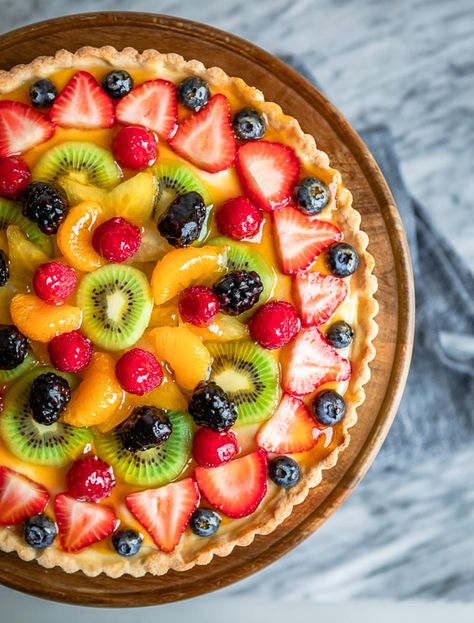 An overhead shot of fresh fruit tart on a wooden stand. Fruit Tart Breakfast, Classic Fruit Tart, Fruit Torte Cake, La Madeleine Fruit Tart Recipe, Best Fruit Tart Recipe, Homemade Fruit Tart, Fruit Tart Dessert, Whole Foods Fruit Tart Recipe, Fruit Tart Pie