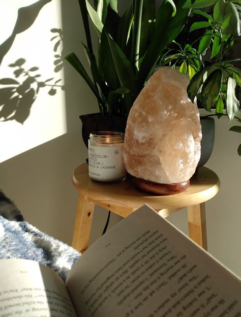 Book open on a cozy chair with a bright, cozy and aesthetic wooden side table with plants, a salt lamp and a lit candle. There is sunlight on the wall. Cozy, warm, aesthetic and bright room inspo & decor. Candle Office Ideas, Feminine Aesthetic Home, Salt Lamp Room, Girl Apartment Aesthetic, Salt Lamp Aesthetic, Therapist Office Aesthetic, Glass Oil Diffuser, Plant Bedroom Aesthetic, Therapist Aesthetic