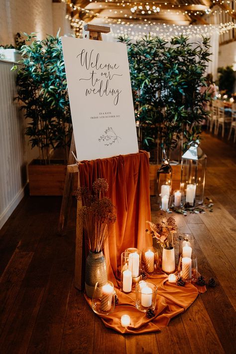 Welcome Sign With Drapery, Ceremony Set Up Indoor, Rust Orange Wedding Decor, Welcome Sign With Candles, Elegant Fall Wedding Ideas Classy, Pillar Candles Decor, Orange Rustic Wedding, Orange Welcome Sign, Wedding Window Decorations