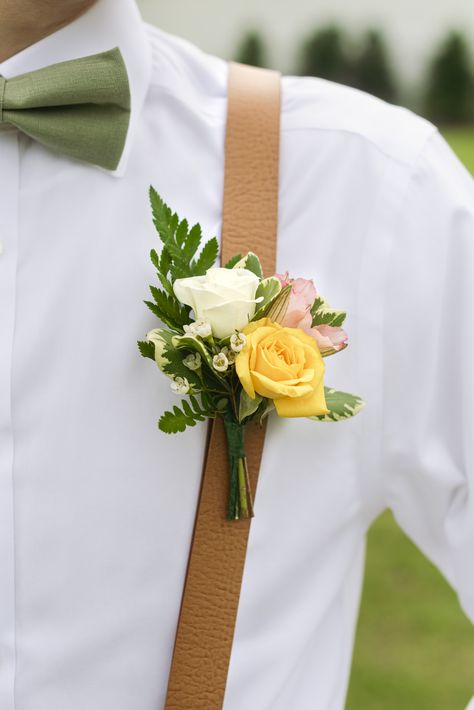 Groomsman or groom wearing colorful boutonniere of yellow white and blush roses with tan suspenders, white shirt and sage green bowtie Yellow And Pink Corsage, Sage Wedding Groomsmen, Yellow Rose Corsage, Bright Yellow Wedding, Pink Groomsmen, Yellow Boutonniere, Groomsman Boutonniere, Boutineer Wedding, Pink Boutonniere