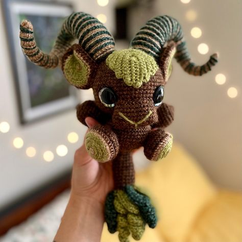 This crocheted Forest Goat would make a wonderful guardian for your houseplant collection. Thoughtfully crafted with two-tone brown and green yarn, textured curled horns, pointed ears, leaf details, and holographic yellow-green eyes, this plushie measures approximately 11" tall from horns to tail.  *Pattern by Grim Grinning Goats" Crochet Mythical Creatures, Brown Amigurumi, Goat Crochet, Forest Crochet, Crochet Goat, Witchy Crochet, Crochet Planter, Crochet Creatures, Houseplant Collection