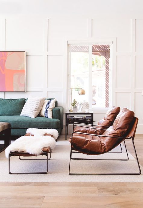 Eclectic modern living room area, green couch pushed against wall with white wainscoting detail. The right of the couch are two brown, modern leather chairs with matching ottomans. Thrown over the ottomans are faux sheepskin throws. Modern Ottomans, Poltrona Design, Leather Ottomans, Wainscoting Wall, Wall Detail, Sofa Green, White Wainscoting, Best Leather Sofa, Sofa Leather