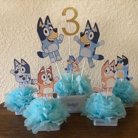 Bluey centerpiece is made with heavy card stock, satin ribbon and blue tissue flower  The main centerpiece is $20 and each character is $4. So what is in the picture is $36  you can purchase any or all parts When purchasing please put the AGE in the note section  It is so cute and would make a great addition to any bluey oarty Bluey Tea Party, Bluey Table Decorations, Bluey Graduation, Twoey Bluey, Bluey Birthday Centerpieces, Bluey Food Ideas Party, Bluey Centerpiece, Bluey First Birthday Party Ideas, Bluey Centerpiece Ideas