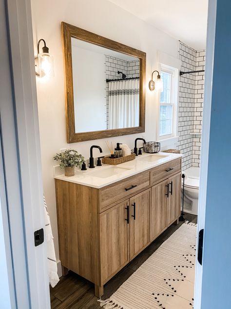 Modern farmhouse double vanity bathroom subway tile dark grout wood grain ceramic tile floor natural wood vanity white quartz top large mirror upcycle sconces turkish bath towels shower curtain boho bath rug @mirrormate #mirror #bathroomremodel #bathroomrenovation #vanity #vanitymirror #naturalwoodfinish #subwaytiles #grout #whiteandwood @moen Shower Tile Ideas With Dark Floors, Small Bathroom With Natural Wood Vanity, One Mirror Double Vanity, Bathroom With Large Vanity, Double Vanity In Small Bathroom, Wood Bathroom Vanity With Wood Floor, Natural Wood Double Vanity Bathroom, Double Vanity For Small Bathroom, Wood Vanity Wood Floor