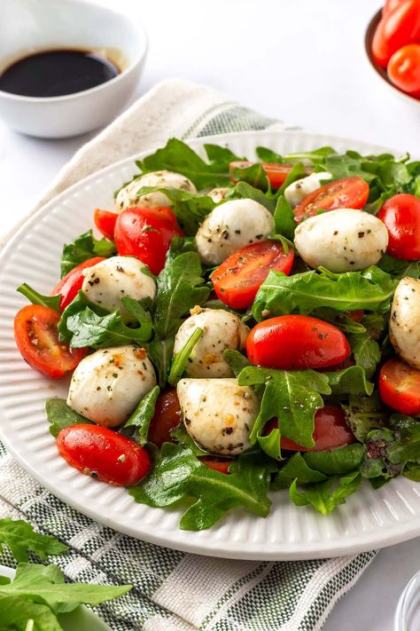 Arugula Caprese Salad on a white plate Arugula Mozzarella Salad, Salad Recipes With Mozzarella Balls, Arugula Caprese Salad, Mini Mozzarella Ball Salad, Salad With Mozzarella Balls, Mozarella Ball, Mini Mozzarella Ball Recipes, Mozerella Ball Ideas, Mozerella Salad