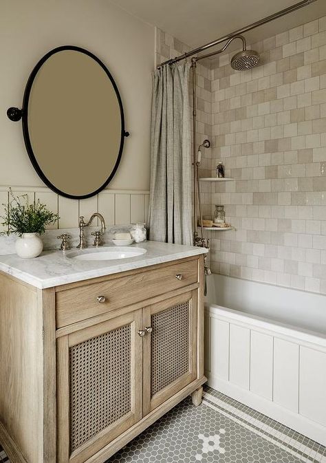 An oval bronze pivot mirror hangs over a beige cane washstand accented with a honed marble countertop finished with a polished nickel hook and spout faucet. Becca Interiors, Rustic Farmhouse Bathroom Ideas, Modern Farmhouse Bathroom Ideas, Timeless Bathroom Design, Bathroom Mirror Design, Farmhouse Bathroom Ideas, Bathroom Stand, Farmhouse Bathroom Design, Rustic Farmhouse Bathroom