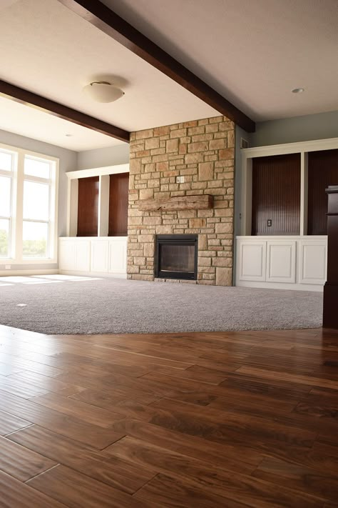 We love how this living room combines cozy and functional flooring. This warm brown hardwood floor pairs perfectly with thick beige carpet, creating a cozy conversation area around the fireplace with stone fascade. For more flooring inspiration visit www.riterug.com #RiteRugFlooing #Livingroomideas #homeinspiration #flooring #carpet #hardwoodflooring #stonefireplace Hardwood And Carpet Combo, Carpet And Hardwood Together Living Room, Wood And Carpet Flooring Combination, Half Carpet Half Wood Living Room, Carpet And Wood Floor Combinations, Carpet Transition Ideas, Carpet And Hardwood Together, Carpet To Hardwood Transition, Carpet Inlay