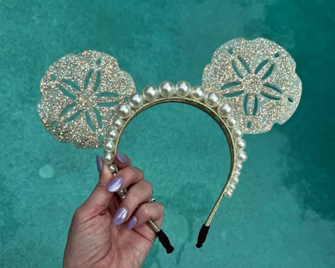 For all my mermaid girlies! These resin sand dollar mouse ears are neutral yet show stopping at the same time. The mouse ears headband is accented with 2 rows of oversized pearls, and the resin sand dollars sparkle with gold flecks and gold glitter. A perfect complement to any mermaid outfit or Ariel inspired look for the parks, these ears are mer-made for you :). Due to the handmade nature of my ears and the artistic quality of resin, each pair will vary slightly, making yours unique and just f Disney Cruise Ears, Avatar Ears, Christmas Mickey Ears, Resin Sand, Pearl Princess, Disney Swag, Diy Disney Ears, Disney Honeymoon, Diy Mickey Ears