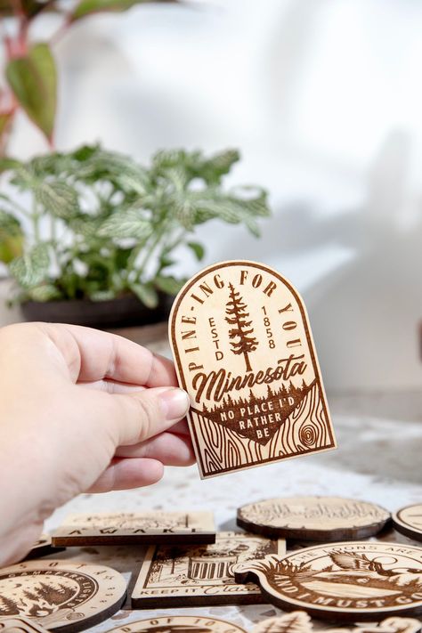 Pine-ing For You Minnesota Engraved Wood Magnet Our Wood Magnets are designed and crafted in-house from quality 1/4 in. engraved plywood. Magnets make great souvenirs from favorite travels, keep track of notes and those pesky to-do lists, or add a little humor to your home or office. +Magnet is about 2.5 in by 3.5 in in size +Quality 1 in. Black Ceramic button Magnet and Attached with a 2-Part Epoxy for strength. +Wood is given a matte finish to seal laser engraving. Please note the color can va Custom Laser Engraving, Cricut Wood Engraving, Travel Souvenirs Ideas, Laser Magnets, Laser Engraving Ideas To Sell, Laser Printer Projects, Wood Laser Engraving Ideas, Laser Engraving Ideas Gifts, Laser Engraver Projects