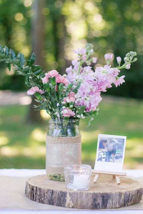 We covered our guests tables with white tablecloths and a burlap runner.  Centerpieces were log slices cut by a family friend , mason jars with burlap and ribbon hot-glued on, polaroid pictures on small wooden easels from Michaels, and a tea candle. Picture Centerpiece Ideas Birthday, Flowers And Picture Frame Centerpiece, Bud Vases On Wood Slice, Picture Frame Flower Vase, Picture Centerpieces, Wild Flower Mason Jar Centerpieces, Wedding Centerpieces Rustic Mason Jars Wood Slices, Simple Table Centerpieces, White Flower Centerpieces