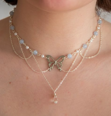 This necklace features delicate pastel blue beads, lustrous pearls, and draped chains, creating a layered, fairy and ethereal look. In the heart of this necklace, a captivating butterfly pendant and a sparkling clear crystal pendant add a touch of timeless beauty.  The layers of draped chains add depth and dimension to the necklace, allowing it to rest gracefully against your neckline, accentuating your natural beauty. The delicate nature of this piece ensures it is suitable for any occasion, from casual outings to formal events, making it a versatile addition to your jewellery collection. Elevate your style with this exquisite accessory, effortlessly blending sophistication with a touch of enchantment.  The pastel blue beads interspersed between the pearls create a harmonious colour palet Fairy Pearl Necklace, Ideas For Necklaces With Beads, Ethereal Jewelry Necklaces, Crystal Necklaces Ideas, Crystal Handmade Jewelry, Fancy Beaded Necklaces, Chain Necklace With Beads, Easy Bead Necklace, Necles Design