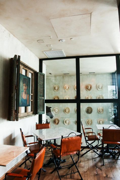 This dining area in Bracero Cocina de Raiz features a wall of steel-framed windows that showcases a view of the staircase. The staircase boasts one of the restaurant's most notable displays, an installation of vintage Bracero hats. Cowboy Restaurant, Cowboy Hat Display, Cowboy Chic, Hat Wall, Hat Display, The Staircase, Vintage Display, Wood Dresser, River House