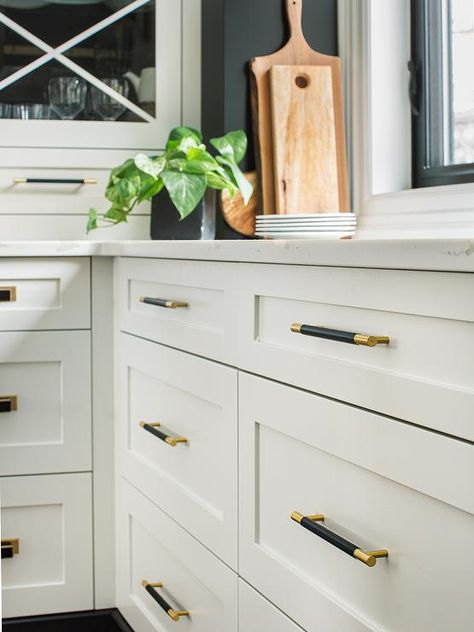 Gold and black pulls accent white shaker kitchen drawers topped with a marble-look countertop. Black And Brass Kitchen Hardware, White Cabinets Black Countertops, Black Kitchen Hardware, Gold Kitchen Hardware, Brass Kitchen Hardware, Gold Cabinet Hardware, Black Cabinet Hardware, White Shaker Kitchen, Black Kitchen Island