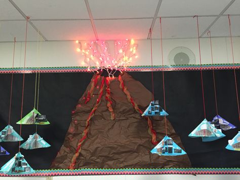 Volcano bulletin board. I used red and orange Christmas lights for the explosion above the volcano crater. I then used red and yellow wired ribbon as the lava oozing down the side. I crumpled the brown paper to establish texture. Volcano foldables hang from the ceiling on both sides like mobiles. Volcano Bulletin Board, Red And Orange Christmas, Dinosaur Bulletin Boards, Survivor Theme, Christmas Lights Inside, Science Bulletin Boards, Classroom Christmas Decorations, Science Room, Stem Elementary