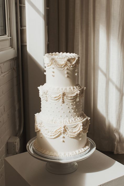 A white three tiered wedding cake with vintage swap piping and polka dots Wedding Cake White Piping, Wedding Cake Aesthetic Simple, Wedding Cake Tiers Sizes, Vintage Theme Wedding Cake, Vintage Wedding Cake Just Married, White Tiered Wedding Cake, Old School Piping Wedding Cake, Modern Vintage Wedding Cake, Three Tier Vintage Cake