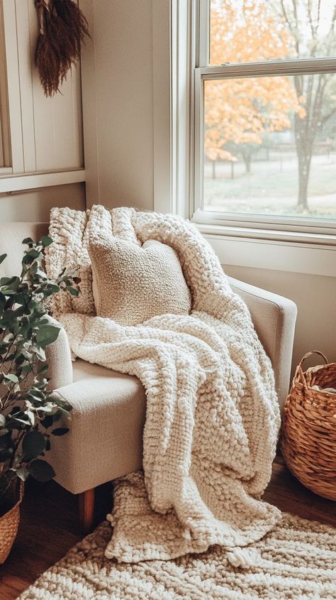 This inviting living space showcases a beautiful blend of cozy neutral textures that create an atmosphere of comfort and relaxation. The oversized knitted blanket drapes invitingly over the chair, while the plush pillow complements the look, enhancing the feeling of warmth. To style a similar setup, consider using chunky knit throws and soft fabrics in complementary shades like cream, taupe, or soft gray to foster a serene environment. Incorporate natural elements, such as a woven basket and gre Cozy Corner Ideas, Neutral Textures, Corner Decoration, Comfy Reading, Serene Environment, Corner Ideas, Chunky Knit Throw, Knitted Blanket, Cozy Reading Nook