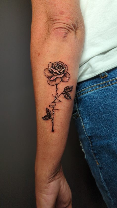 Blackwork floral tattoo with lettering in the stem Placement: back of forearm Rose Tattoo With Letter Stem, Rose With Writing Stem Tattoo, Rose Stem Tattoo Words, Long Stem Rose Tattoo Forearm, Name In Rose Stem Tattoo, Men’s Forearm Tattoo Ideas Rose, Rose Quote Tattoo Forearm, Rose Stem Tattoo, Rose Stem