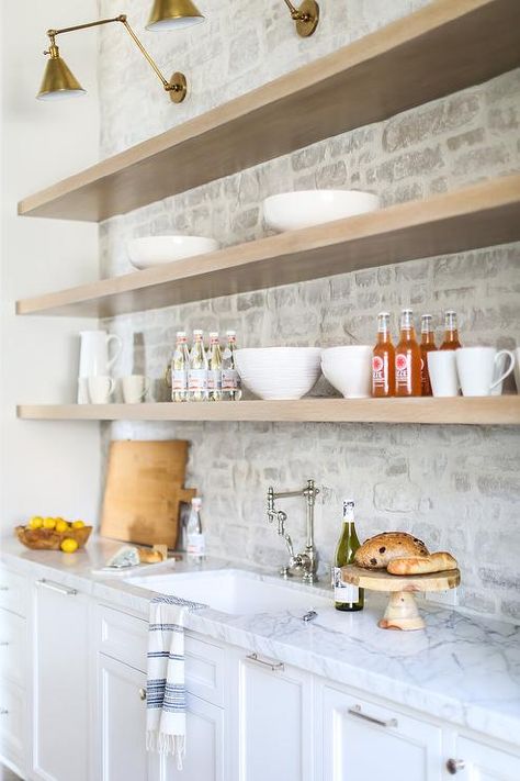 Vintage brass swing arm sconces are mounted to a faded red brick wall over gray wash wooden floating shelves fitted above a sink with a vintage swing arm faucet. Brandon Architects, Brick Kitchen Backsplash, Brick Backsplash Kitchen, Stone Backsplash Kitchen, Travertine Backsplash, Dirty Kitchen, Brick Kitchen, Brick Backsplash, Stone Backsplash