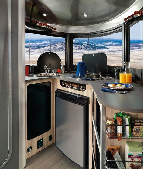 The kitchen features a stove, sink, microwave, and refrigerator, as well as lots of smart storage. Rv Interiors, Airstream Basecamp, Airstream Living, Airstream Bambi, Lightweight Trailers, Airstream Rv, Airstream For Sale, Airstream Travel Trailers, Air Stream