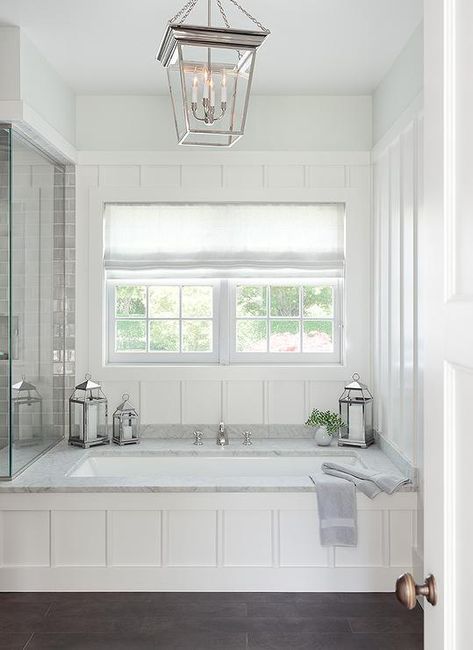 The perfect place to relax, this stunning cottage bathroom boasts a wainscoted drop in bathtub accented with a marble deck a polished nickel tub filler fixed in front of a board and batten wall framing a window dressed in a white linen shade lit by a Small Cornice Hanging Lantern. Bathtub Surround, Built In Bathtub, Marble Tub, Drop In Bathtub, Bathtub Remodel, Cottage Bathroom, Master Bath Remodel, Trendy Bathroom, White Rooms