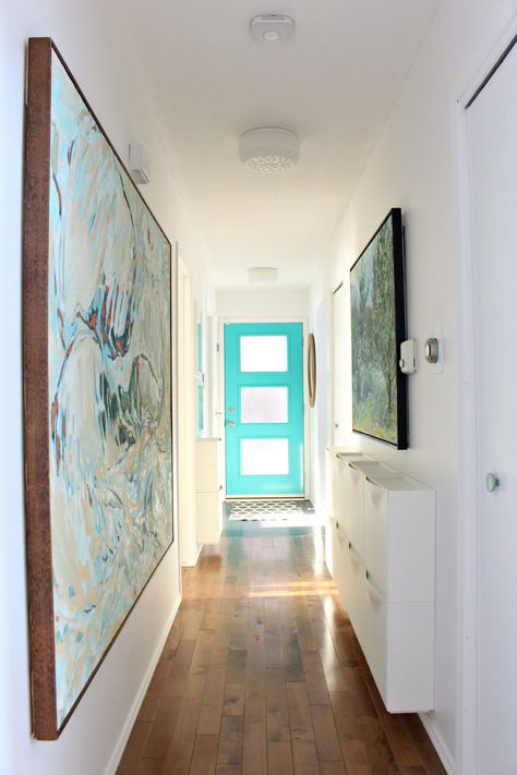 Colorful but small entryway with turquoise mid-century modern style front door, bold and large scale artwork, and a genius narrow entryway storage solution: 10 IKEA TRONES shoe cabinets, which are a shallow storage cabinet that are used in this hallways for storing dog leashes, hats, mitts and scarves. #trones #storage #smallspacestorage Narrow Entryway Storage, Colorful Entryway, Trones Ikea, Entryway Storage Ideas, Ikea Trones, House Entryway, Aqua Inspiration, Entryway Storage Cabinet, Turquoise Door