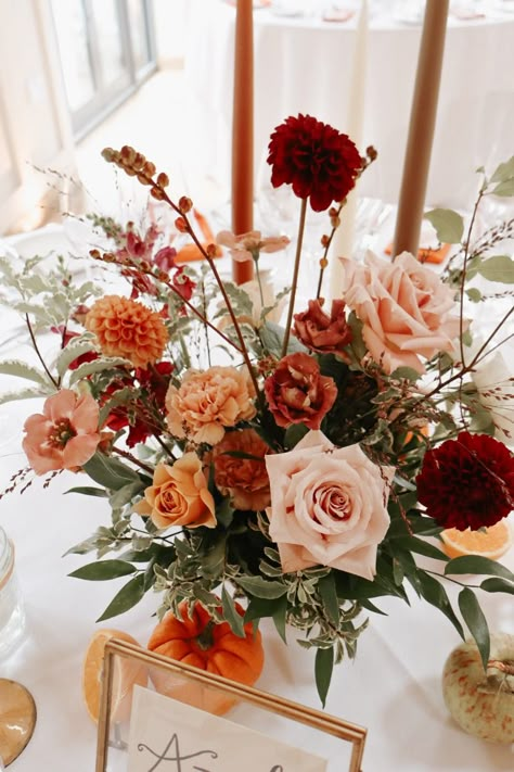 These beautiful, textural, autumnal centrepieces incorporate quicksand rose, dahlia black fox, dahlia cornel bronze, lisianthus rosanne deep brown, golden mustard rose, caramel carnation, lisianthus bohemian choco, red snapdragon, crocosmia and delicate grasses. We have also incorporated fruit into the design, enriching our colour palette and creating even more texture within the tablescape. Terracotta Flowers Wedding Table, Terracotta Wedding Centerpieces Flowers, Red And Terracotta Wedding, Terracotta Wedding Flowers Centerpiece, Autumn Wedding Flowers Table, Autumnal Centrepieces, Fall Boho Wedding Centerpieces, Wedding Flowers Autumn, Caramel Carnation