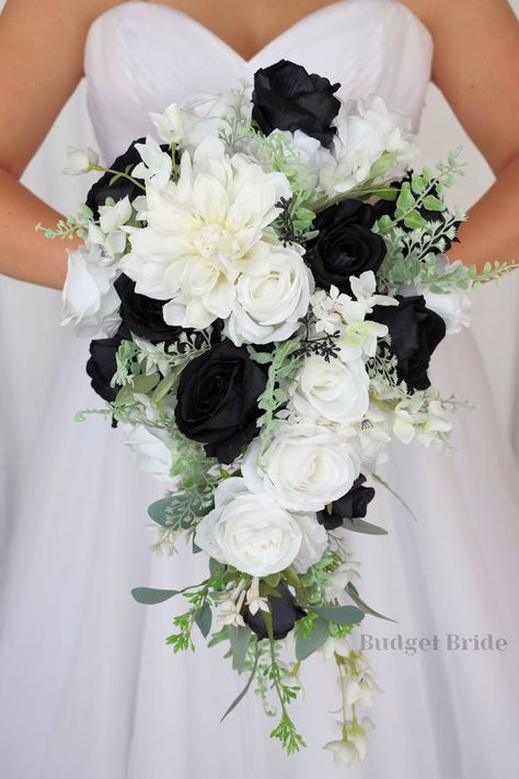 This is a cascading brides bouquet with white dahlia, white and black roses and greenery. All of our wedding bouquets are made with artificial wedding flowers. Wedding Black And Greenery, Black White Gold Wedding Bouquet, Black And Sage Wedding Bouquet, Black And White Wedding Bride And Groom Table, White Roses Bridal Bouquet With Greenery, Modern Black And White Wedding Bouquet, White And Black Rose Bouquet, Black Wedding Floral Arrangements, Wedding Flowers For Black Dresses