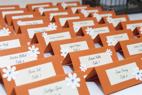 DIY name cards/table seating for wedding in orange. Printed the names in pearl sheen paper and pasted on folded orange card stock. Glued white flowers in random corners. Diy Table Name Cards, Diy Wedding Name Place Cards, Table Numbering, Diy Name Cards, Homecoming 2023, Wedding Table Name Cards, 20th Bday, Edgy Bridal, Wedding Seating Cards