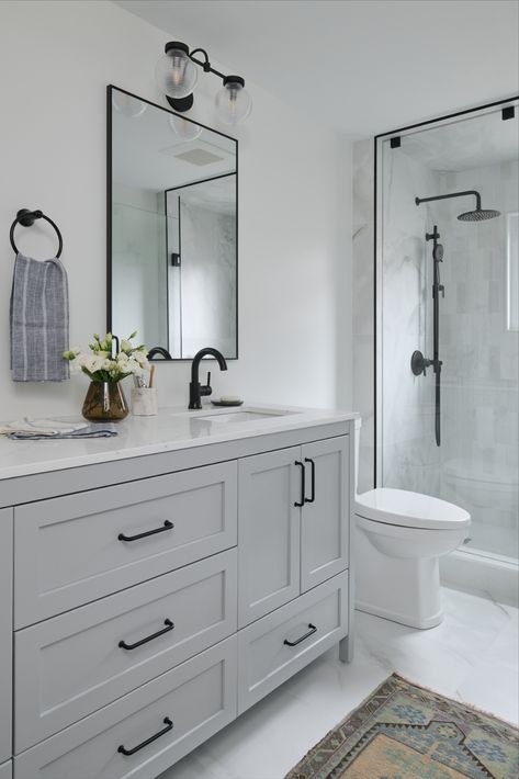 White washroom with warm grey double vanity and black plumbing fixtures with tiled shower and glass enclosure Farmhouse Washroom, Black Plumbing Fixtures, Black Fixtures Bathroom, White Washroom, Black Hardware Bathroom, Black Bathroom Fixtures, Light Grey Bathrooms, Grey Bathroom Cabinets, Gray And White Bathroom