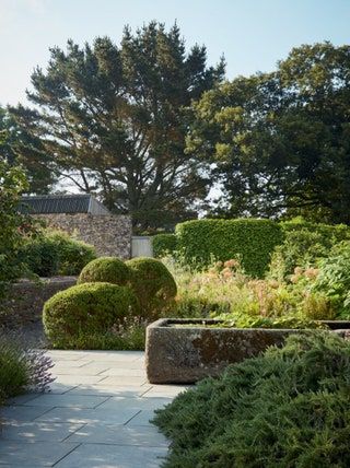 An old stone trough in this area is a nod to the sites agricultural heritage. Tropical Courtyard Garden, Southern Landscaping, Tropical Courtyard, Stone Trough, Plum Varieties, In Tune With Nature, Devon House, Dan Pearson, Formal Garden Design